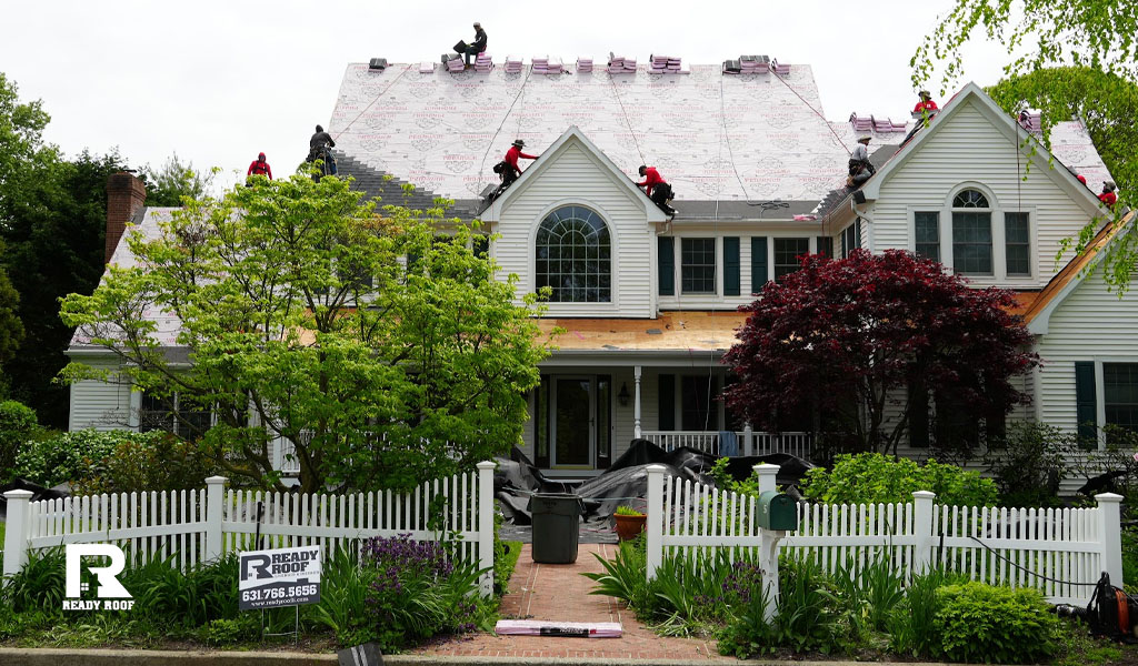 A large crew works on a residential roof, representing the scale of your gutter installation cost on long island.