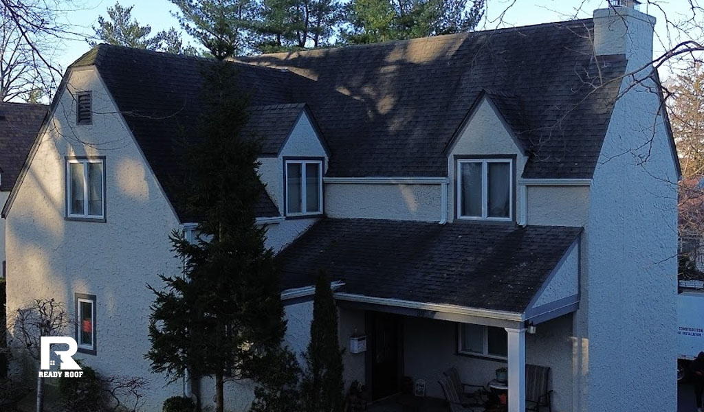 A professional roofing team and service truck preparing a large residential home for a necessary roof flashing repair.