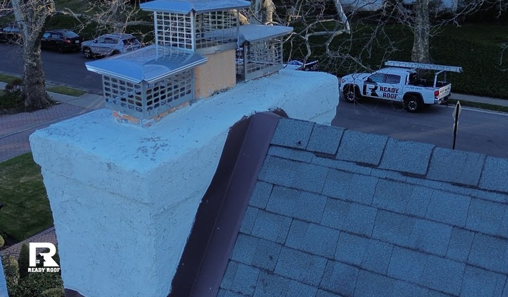 Close-up of a white chimney with metal caps and brown metal details, demonstrating a completed roof flashing repair.
