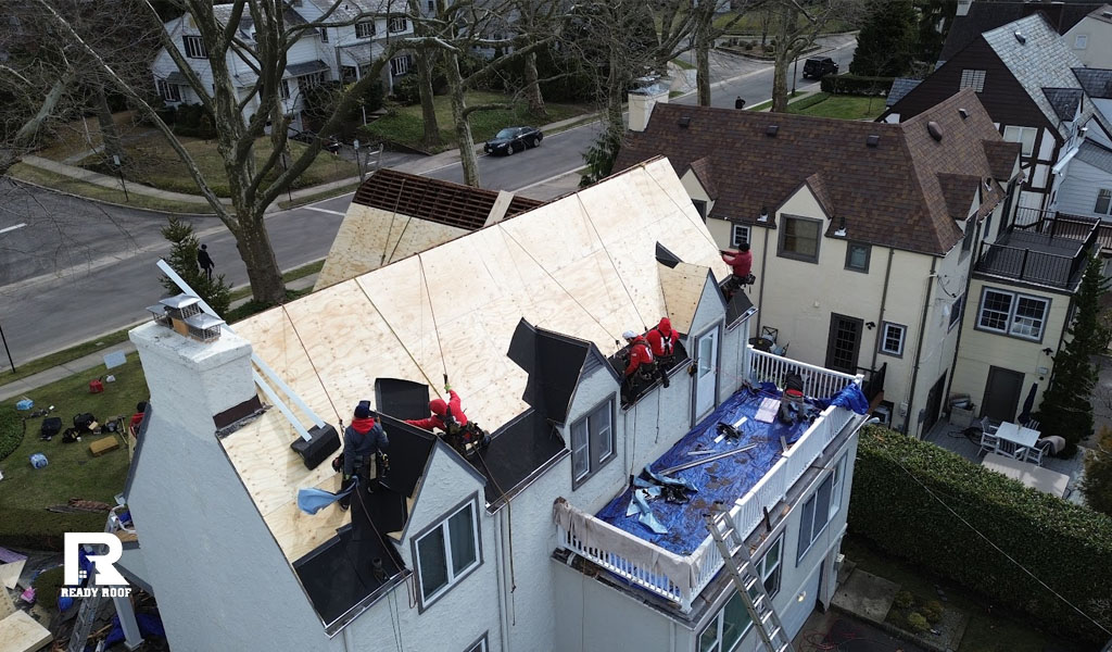 Workers secured by ropes install new roof sheathing. Crucial context for when should you replace your roof.