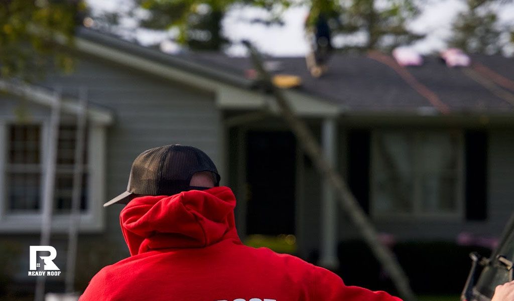 A Ready Roof worker in red evaluates a home to determine the roof repair cost on Long Island