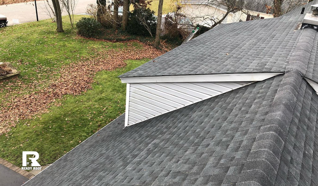 Aerial view of dark roof shingles and white dormer siding, representing siding installation cost on long island.