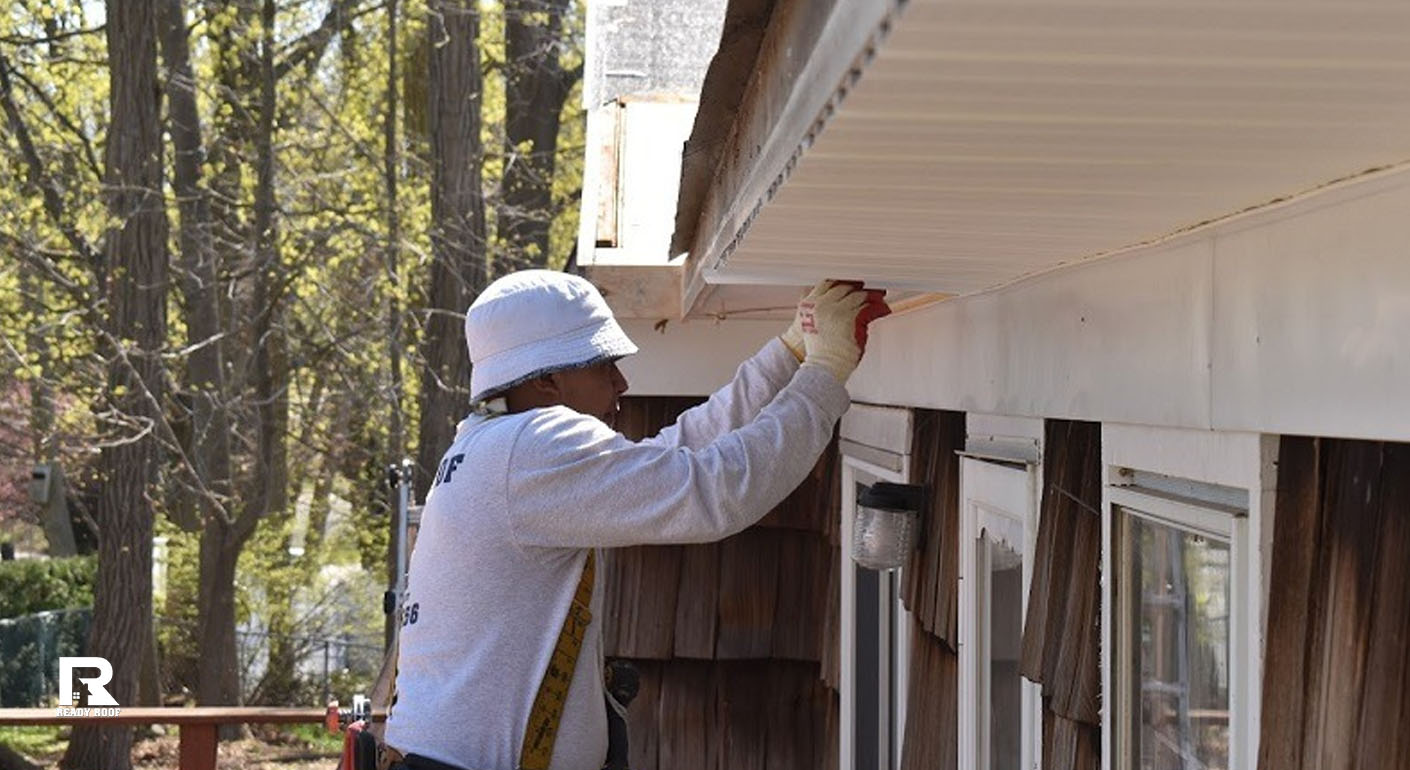 A worker installs white exterior soffit, demonstrating the labor involved in siding installation cost on long island.